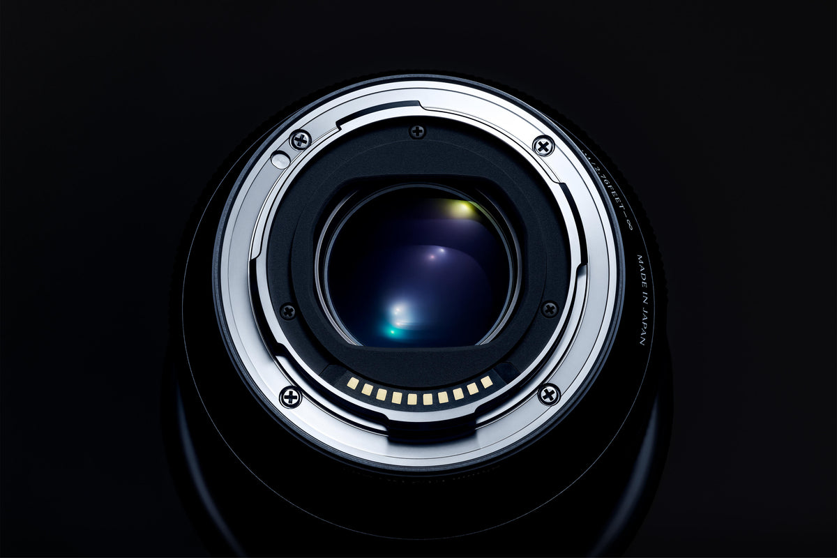 Close-up of the rear mount of a Sigma camera lens, highlighting the metal bayonet, electronic contacts, and optical glass elements against a black background.