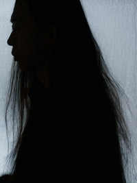 Silhouetted profile of a woman with long dark hair against a softly lit pale background.