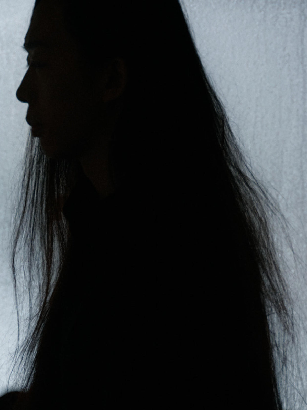 Silhouetted profile of a woman with long dark hair against a softly lit pale background.